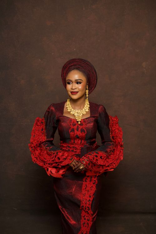 Free Portrait of a Nigerian bride in burgundy lace gown and gele headtie adorned with gold jewelry. Stock Photo