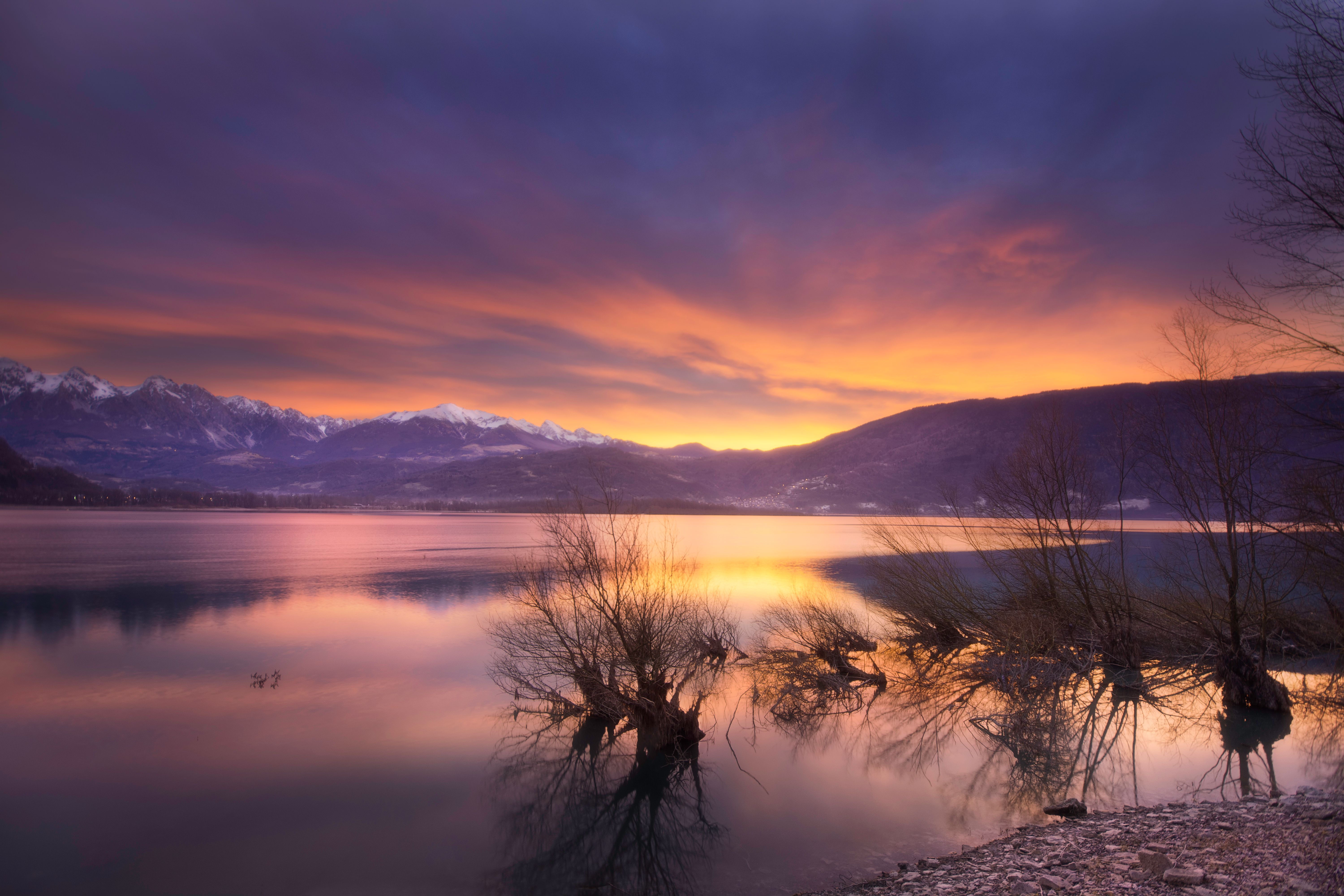 Breathtaking view of the sunset reflecting on Santa Croce Lake with snow-capped mountains in Veneto, Italy.