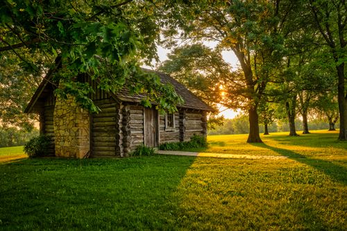 Free A picturesque log cabin surrounded by lush trees and vibrant grass at sunset in Stockholm, Wisconsin. Stock Photo