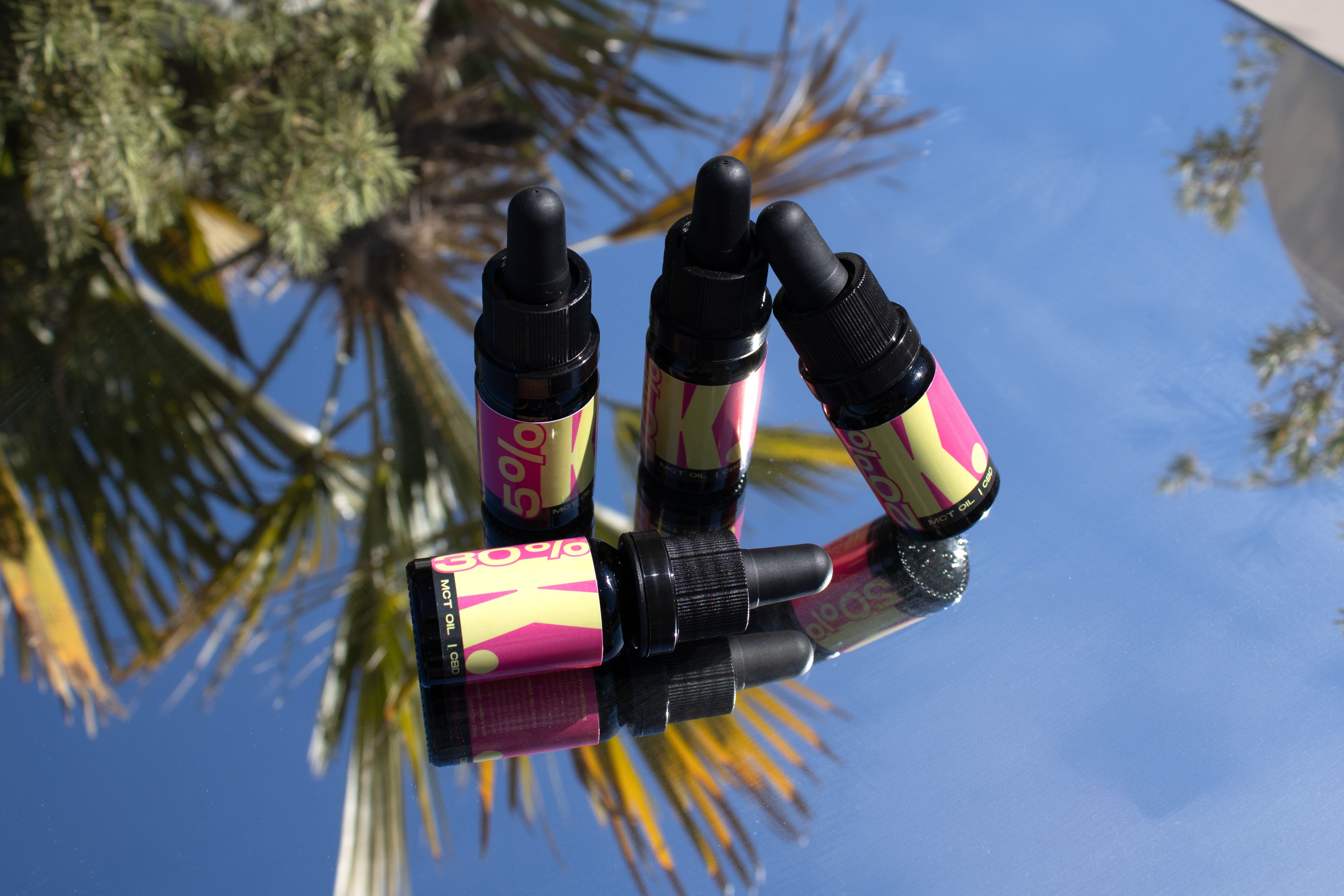 Vibrant CBD oil bottles on a reflective surface with palm tree reflections, capturing natural beauty.
