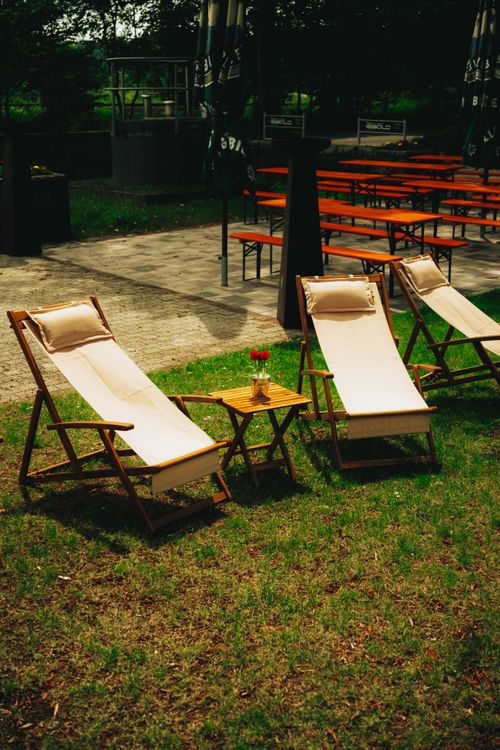 Free Relaxing outdoor setting with wooden lounge chairs and tables, ideal for summer leisure in a beer garden. Stock Photo