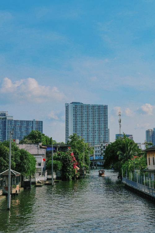 Free Tranquil canal in Bangkok with modern skyscrapers and lush greenery under a clear blue sky. Stock Photo