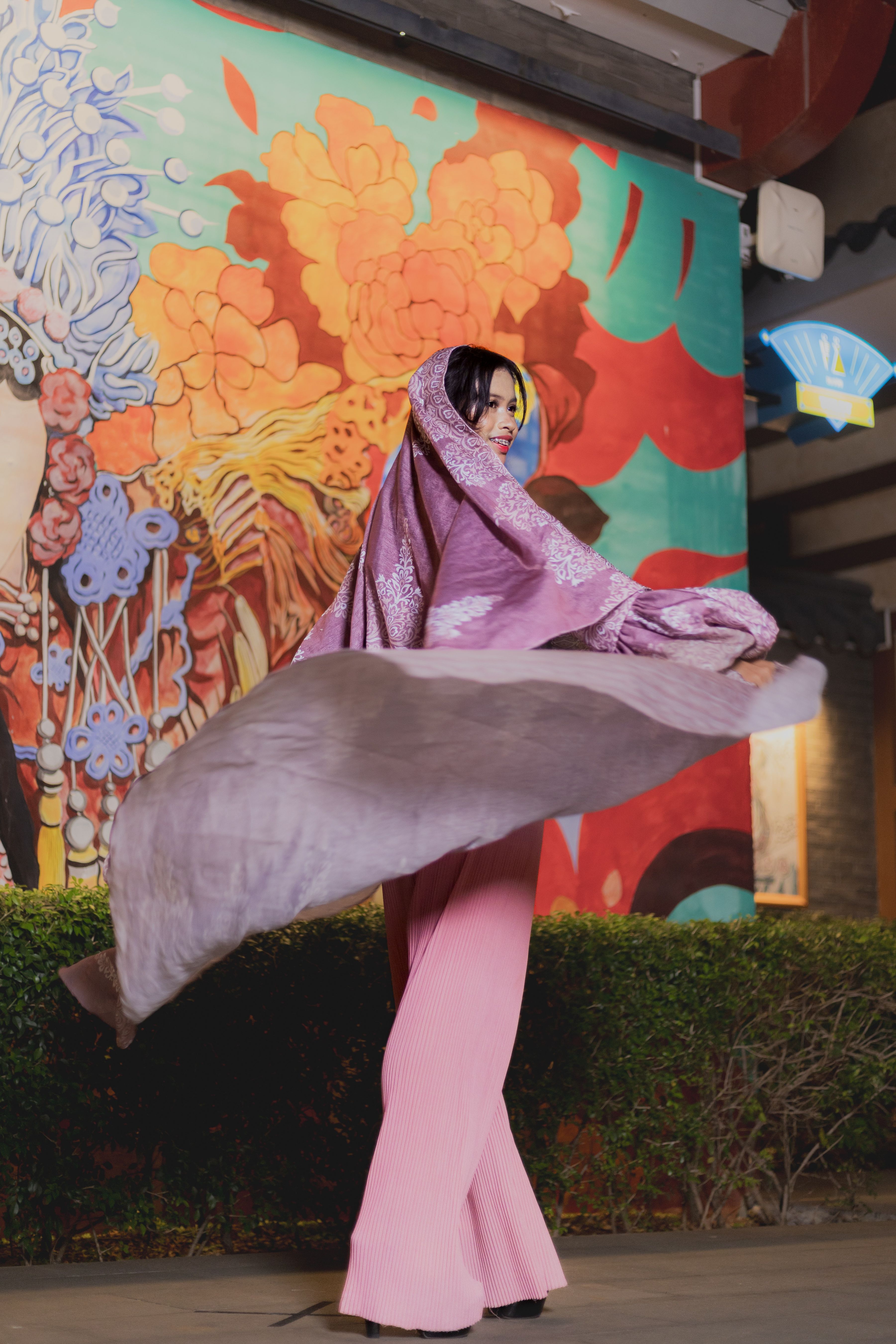 A woman in flowing attire dances gracefully against a colorful mural backdrop.