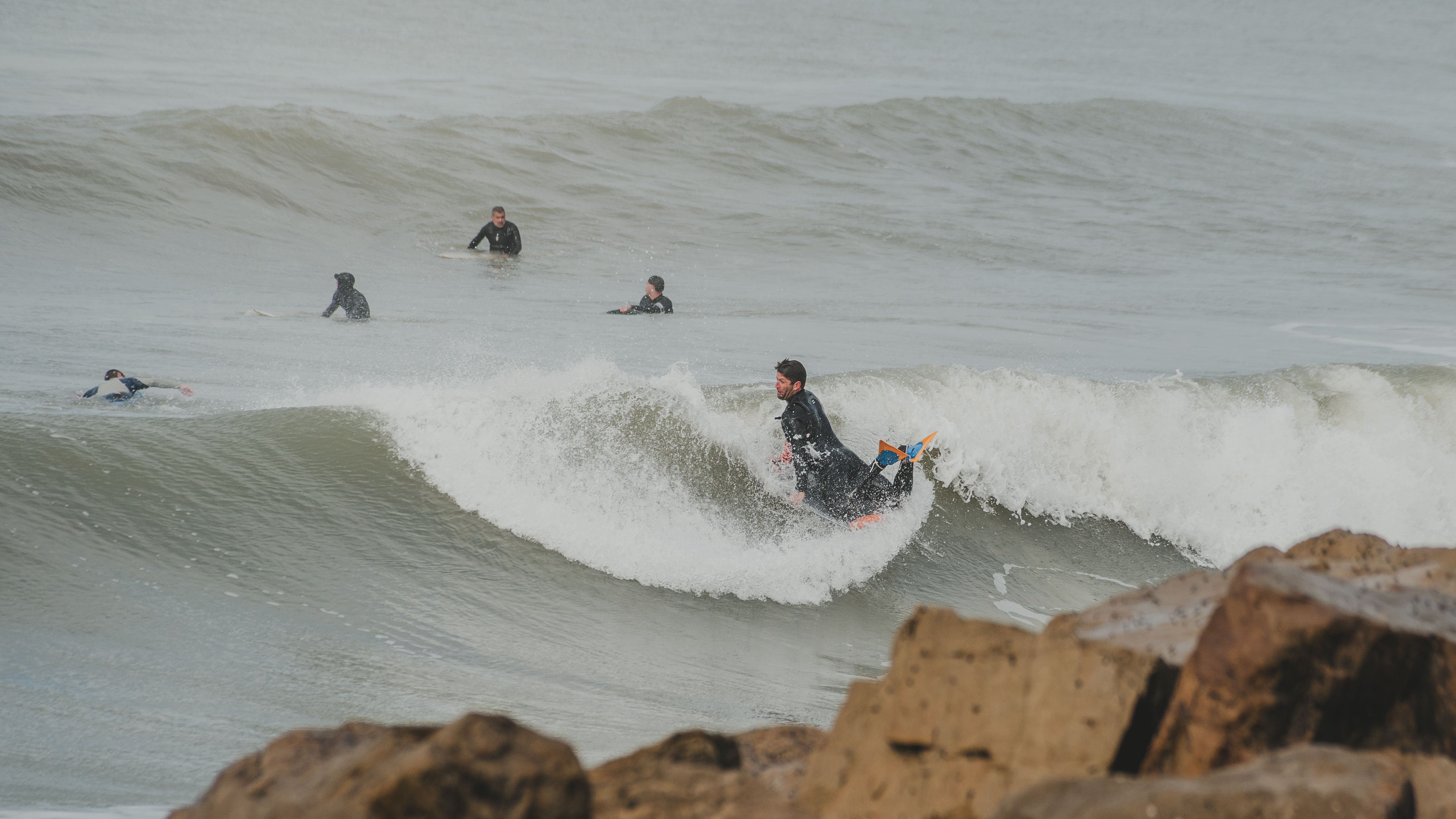 Group of surfers catching waves near a rocky shoreline, enjoying a day of adventure.