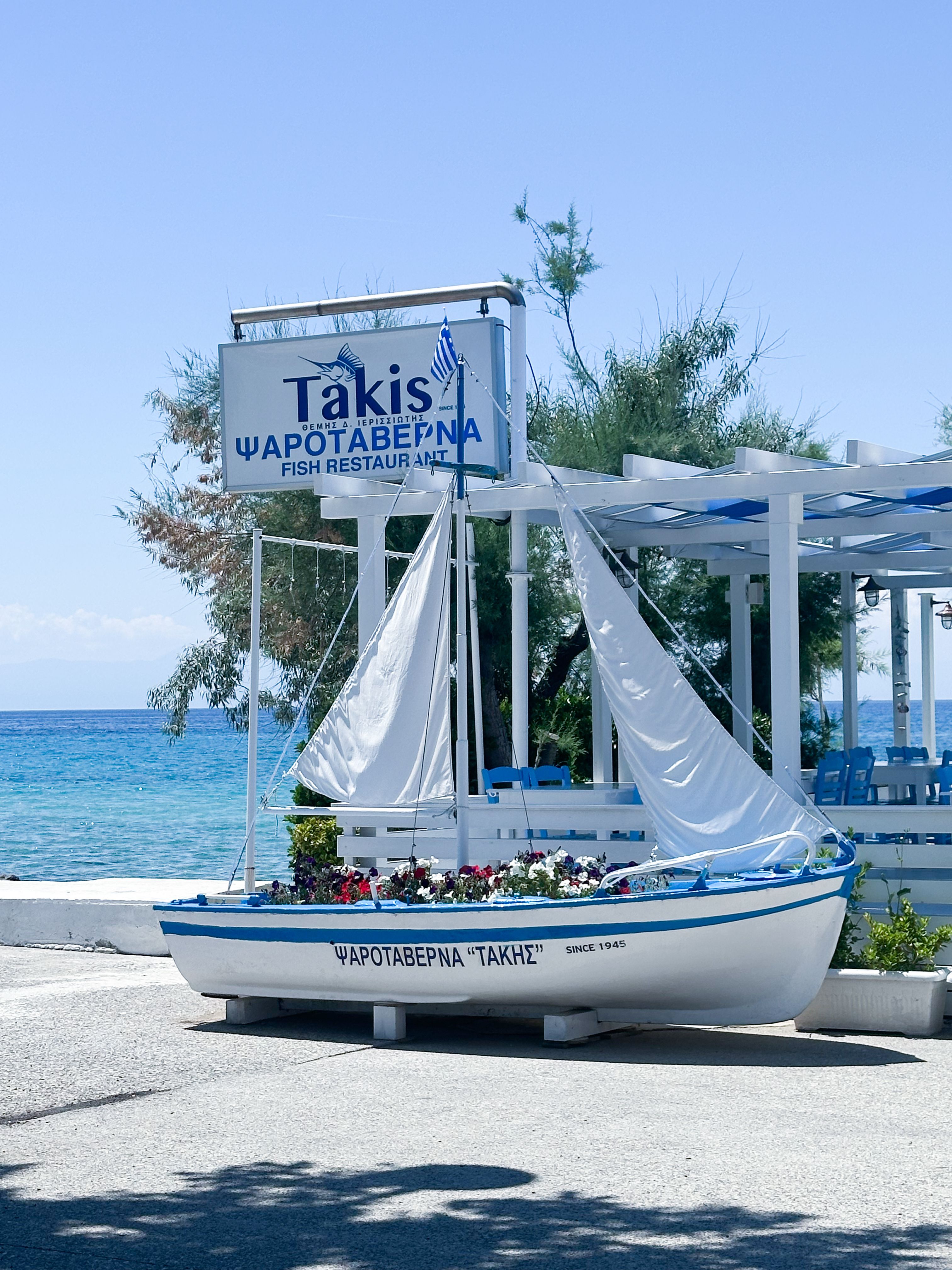 Traditional Greek taverna with blue chairs set by the sea, the kind of spot where dakos arrives as a starter