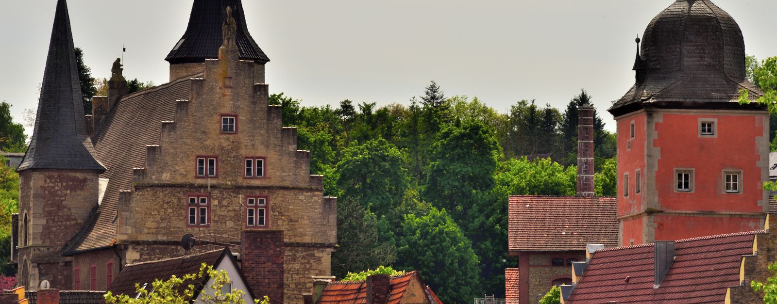 Charming view of castle architecture in Ochsenfurt, Germany amidst green foliage.