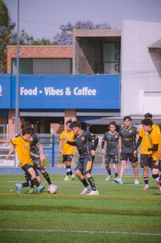 Teenagers playing soccer on an urban field near a cafe, showcasing team spirit and competition.