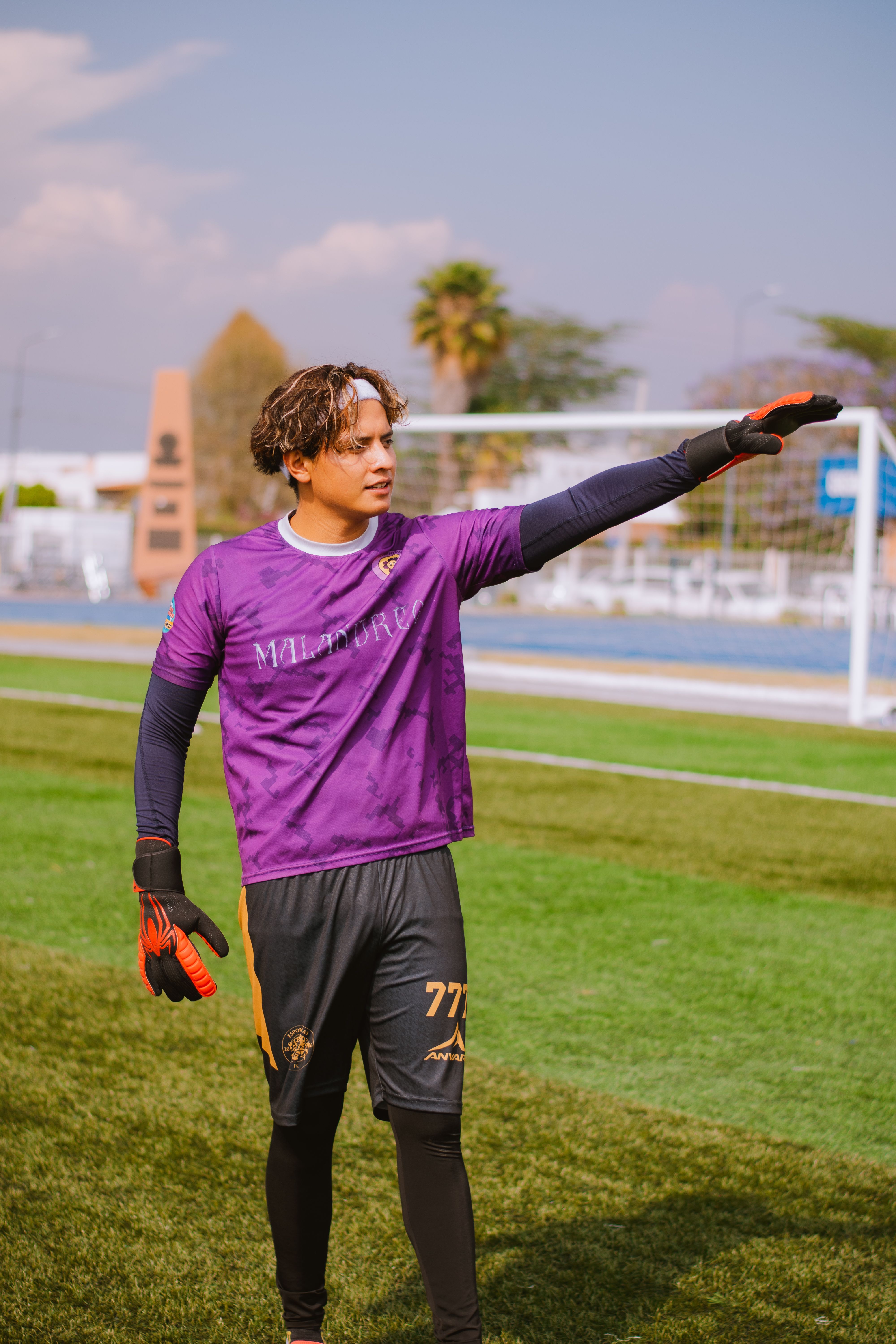A young goalkeeper in purple jersey guides teammates on the soccer field during a sunny day.