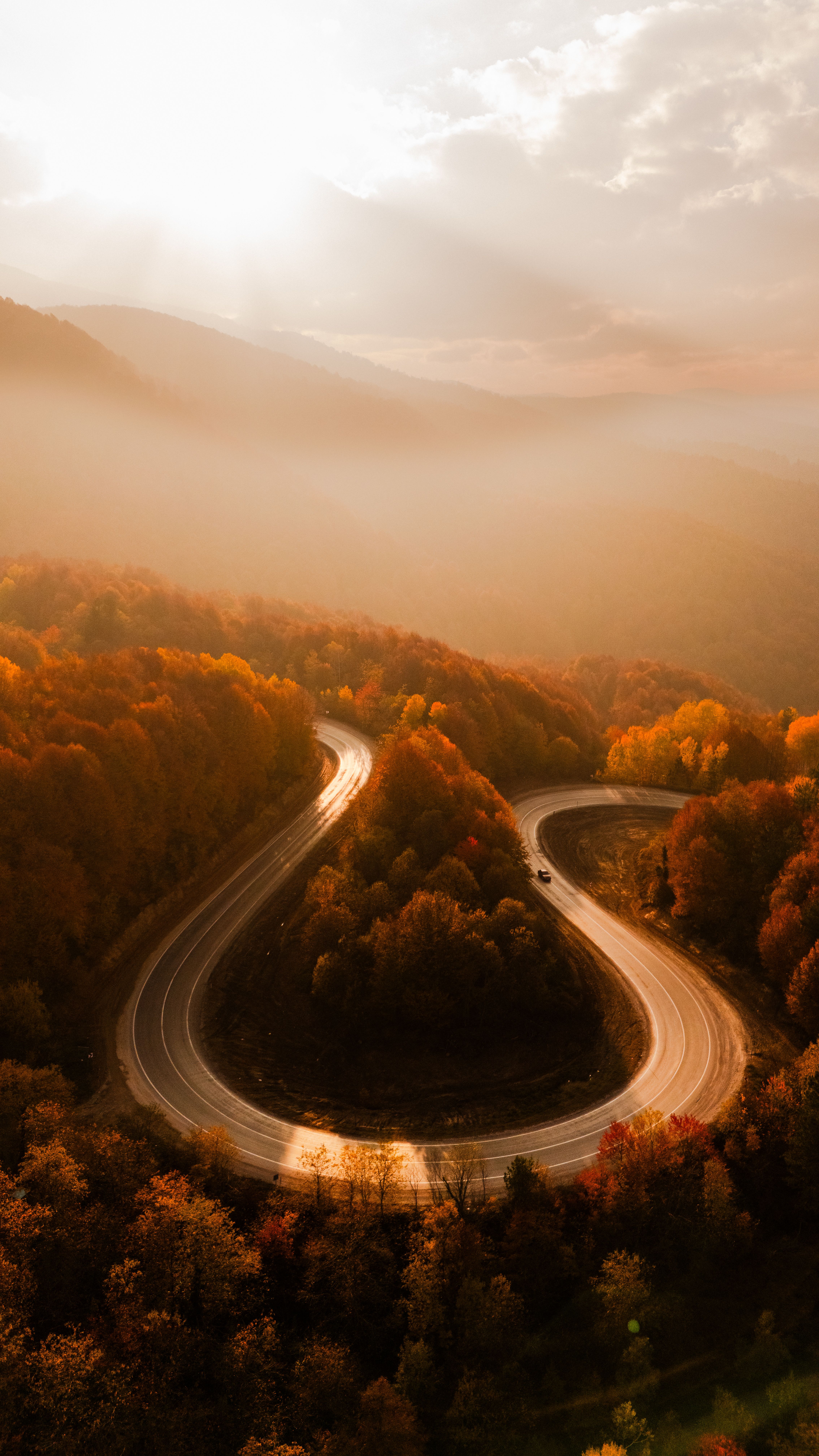 Aerial view of a winding road through vibrant fall foliage at sunrise in Kütahya, Türkiye.