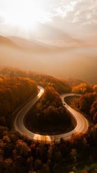 Aerial view of a winding road through vibrant fall foliage at sunrise in Kütahya, Türkiye.