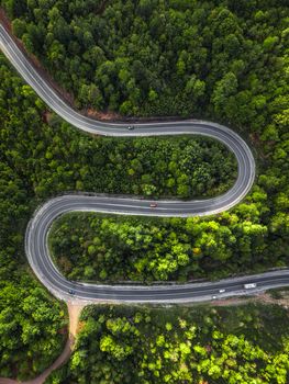 Aerial view of a winding road cutting through dense green forest, capturing natural beauty and adventure.