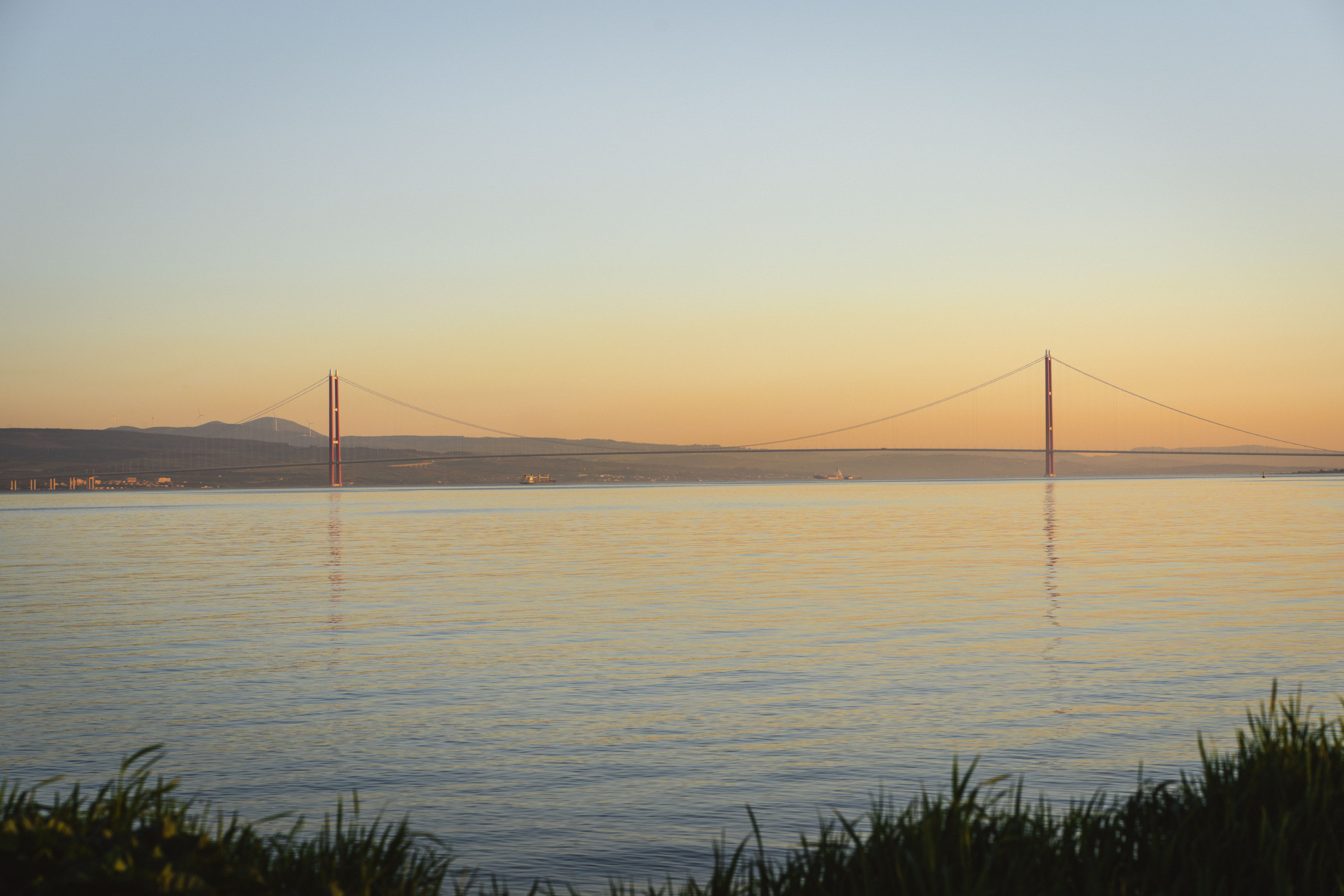 Scenic view of Çanakkale Bridge at sunset reflecting over calm waters.