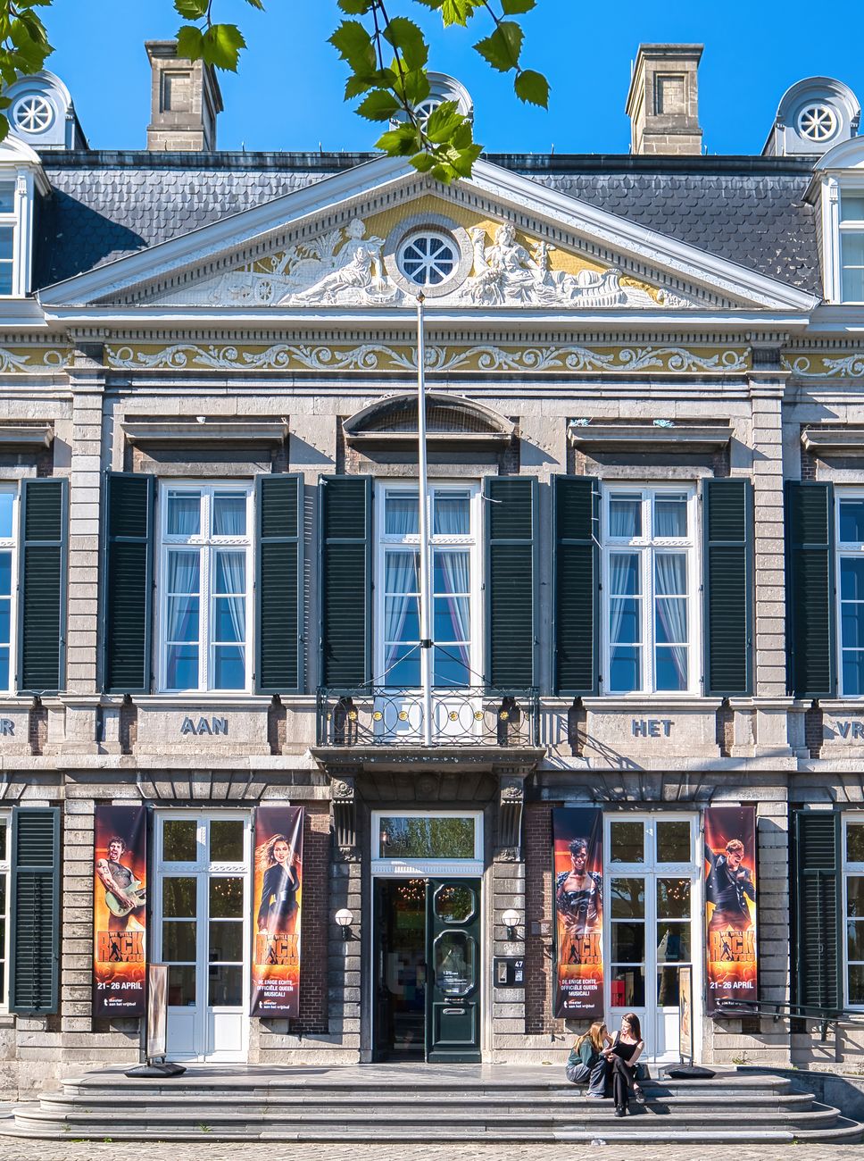 Vooraanzicht van een prachtig historisch theatergebouw in Maastricht met grote ramen en kleurrijke posters.