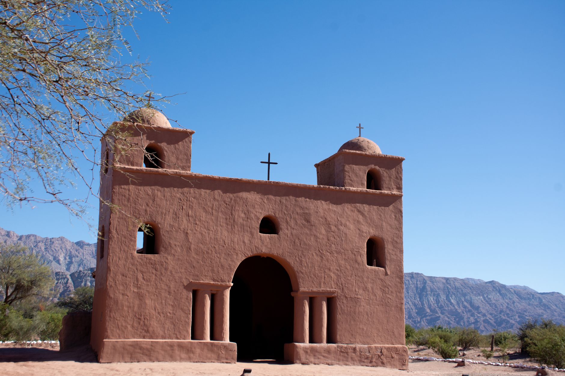Rustic adobe church set against the scenic mountains of Argentina under a clear blue sky.