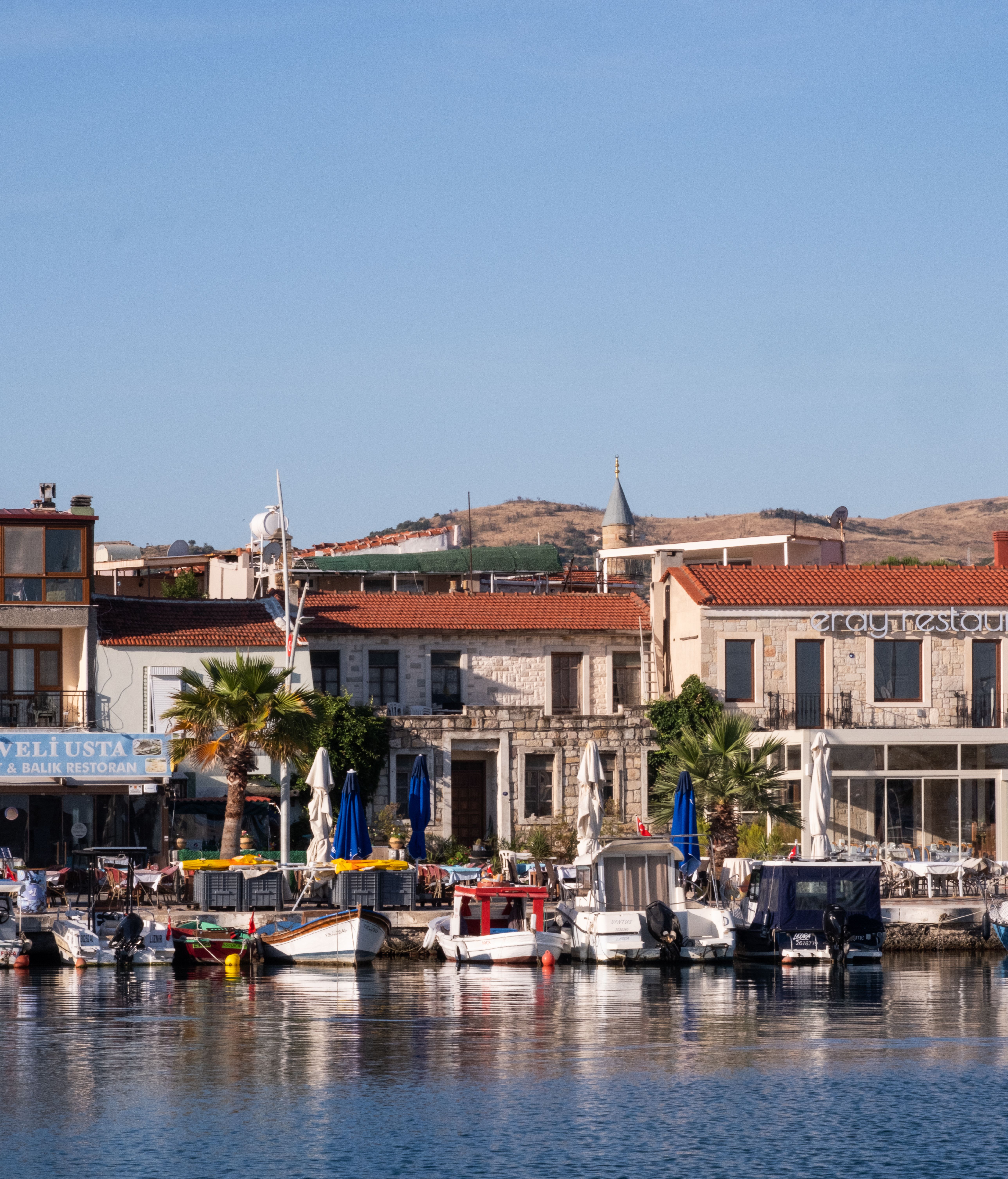 Charming marina scene at Foça, İzmir, Türkiye, with boats, stone buildings, and blue sky.