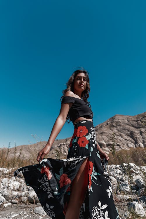 Woman in Black and Red Floral Dress Standing on Rocky Ground