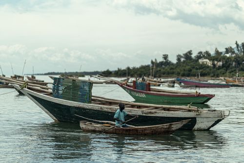 Free Wooden fishing boats float peacefully on a calm lake, with a fisherman paddling in a small canoe. Stock Photo