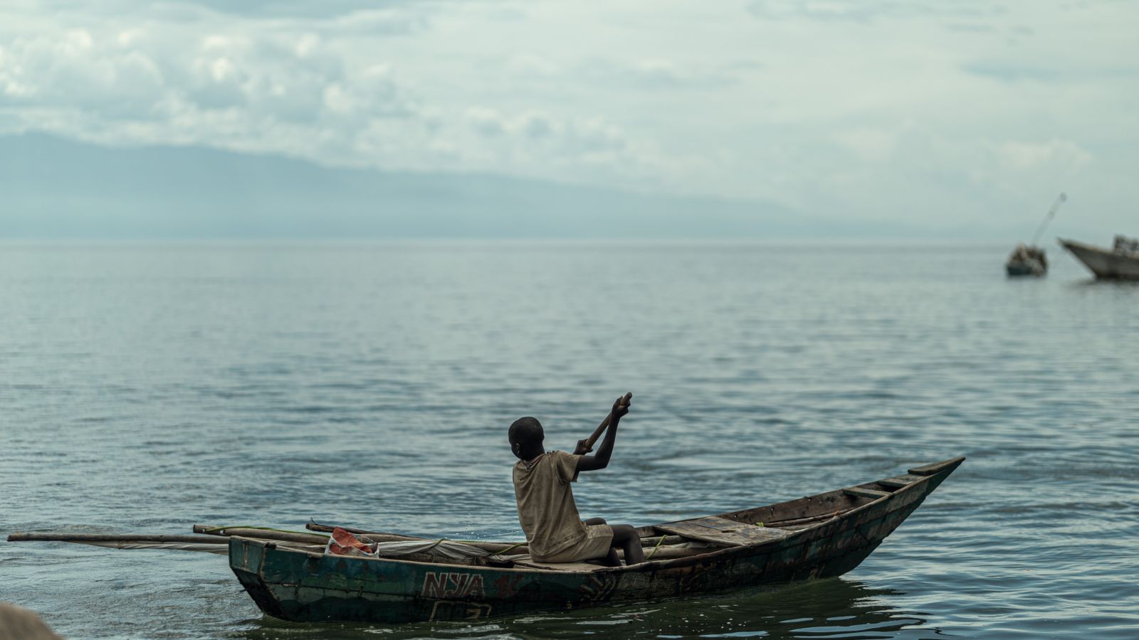 Solitary fisherman in wooden boat on tranquil lake, Burundi