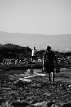 Two men walking on a beach shore, captured in a black and white photograph.