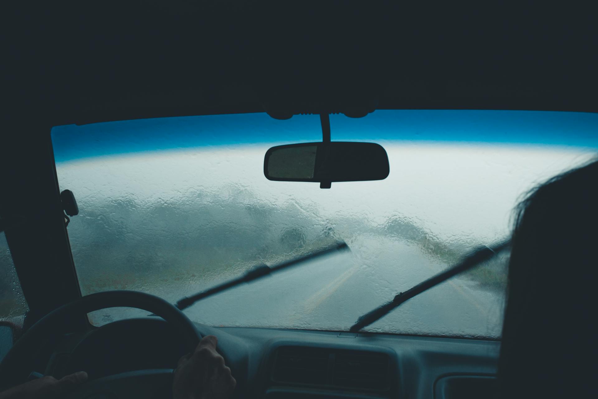 Interior car view on a rainy day with water droplets on windshield and wipers in motion.