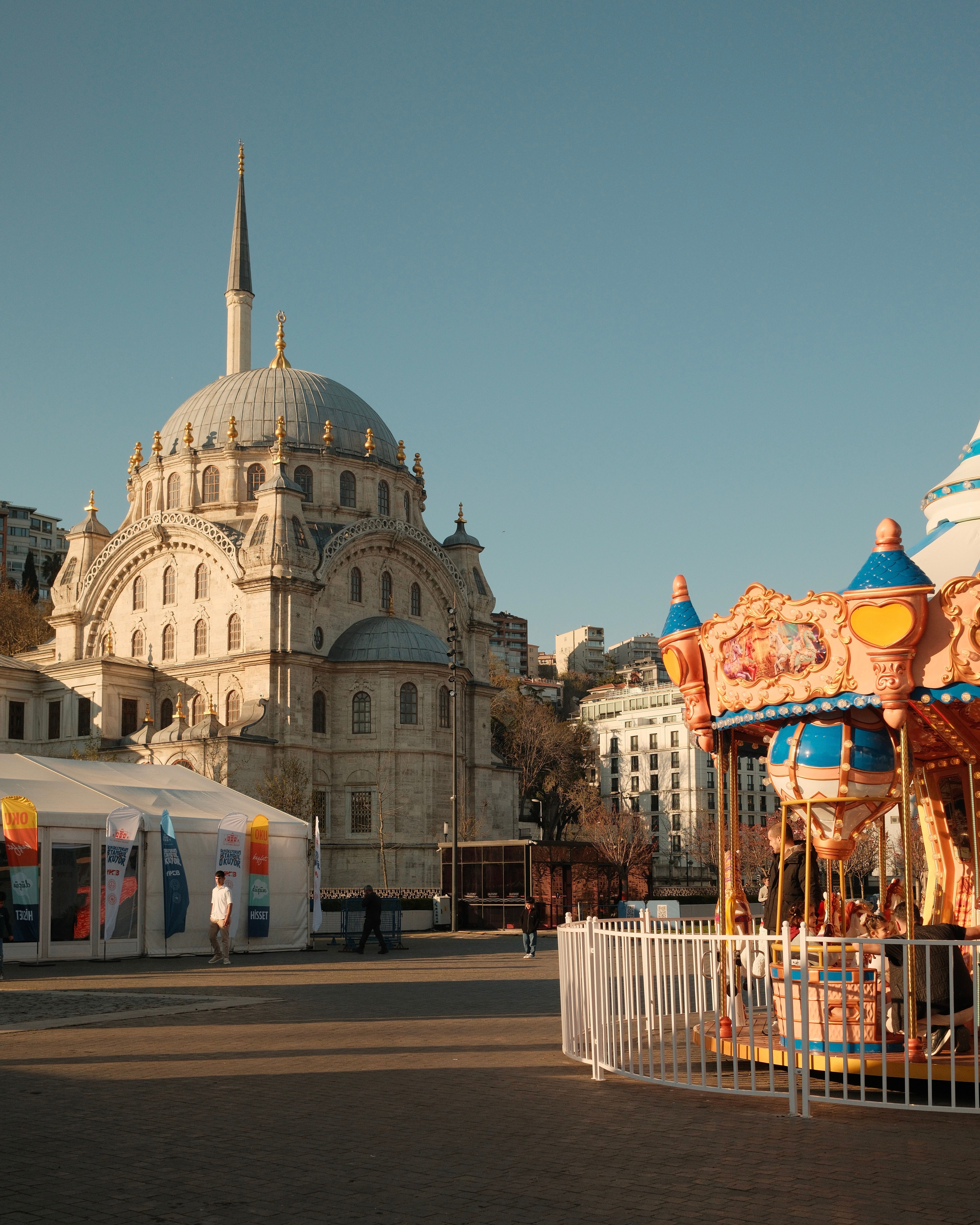 Sunny day in Istanbul showcasing a historic mosque alongside a colorful amusement park carousel.