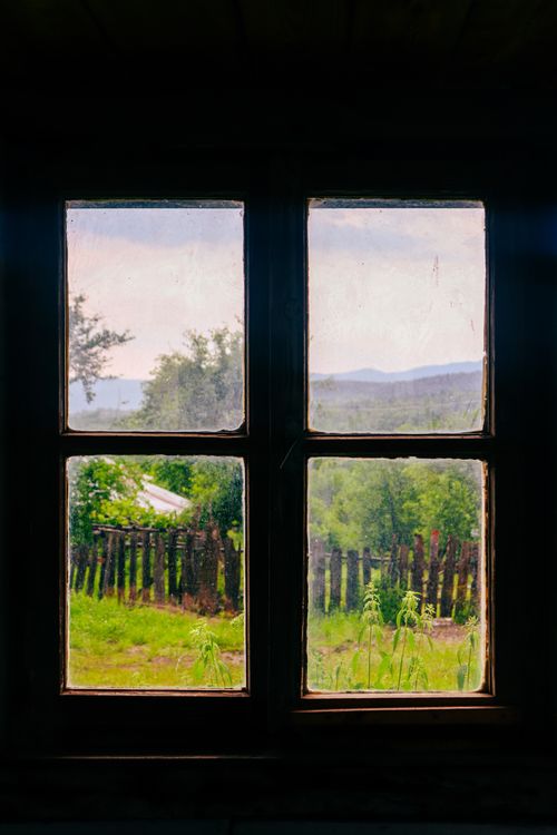 Free A scenic view through a rustic window, overlooking a lush green landscape and wooden fence. Stock Photo