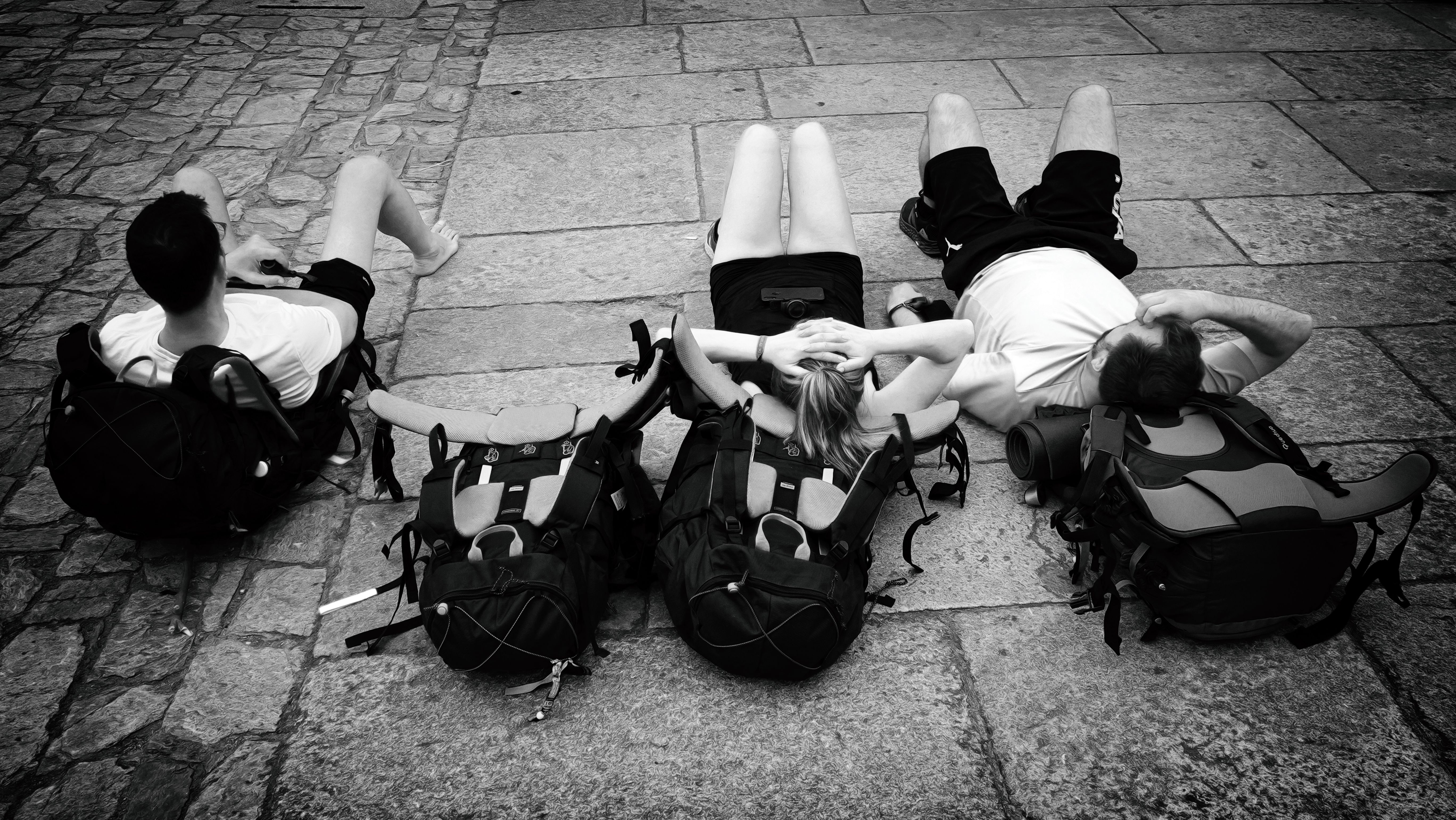 Three travelers resting with backpacks on a cobblestone street, embracing a moment of relaxation outdoors.