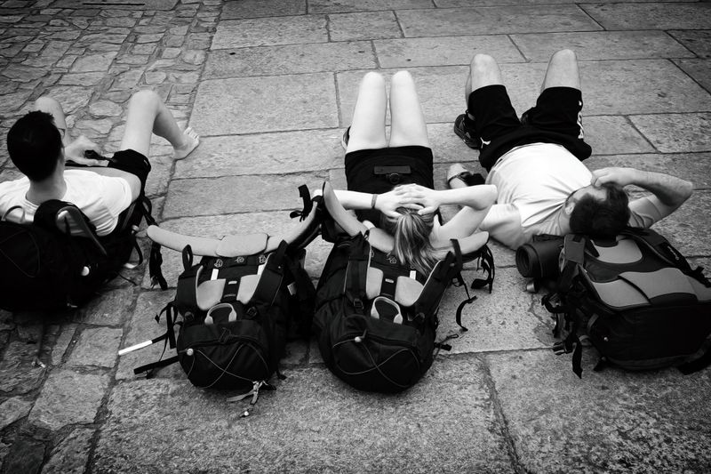 Three travelers resting with backpacks on a cobblestone street, embracing a moment of relaxation outdoors.
