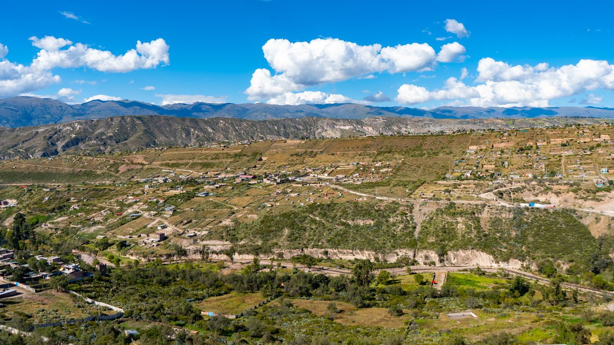 Bolivian village on a green mountain slope under a bright blue sky
