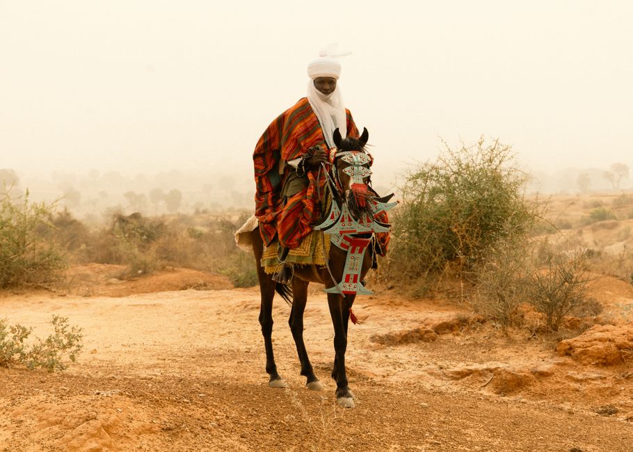 A traditional horseman with colorful attire riding through a desert landscape, embodying cultural heritage.