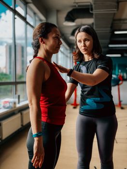 Female fitness trainer guides a client in a modern gym setting for optimal workout alignment.