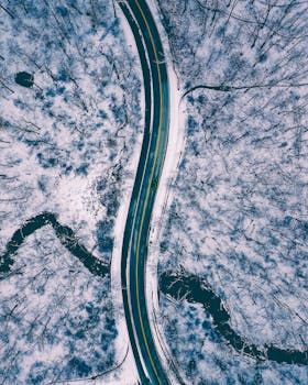 从迷人的鸟瞰图中，蜿蜒的道路穿过白雪覆盖的森林，展现出冬天的宁静之美