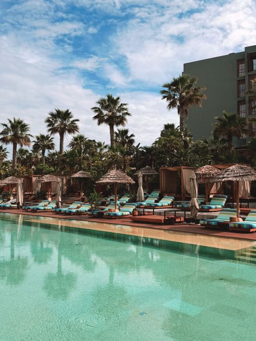 Free Relaxing tropical resort poolside scene with cabanas and palm trees under a bright blue sky. Stock Photo