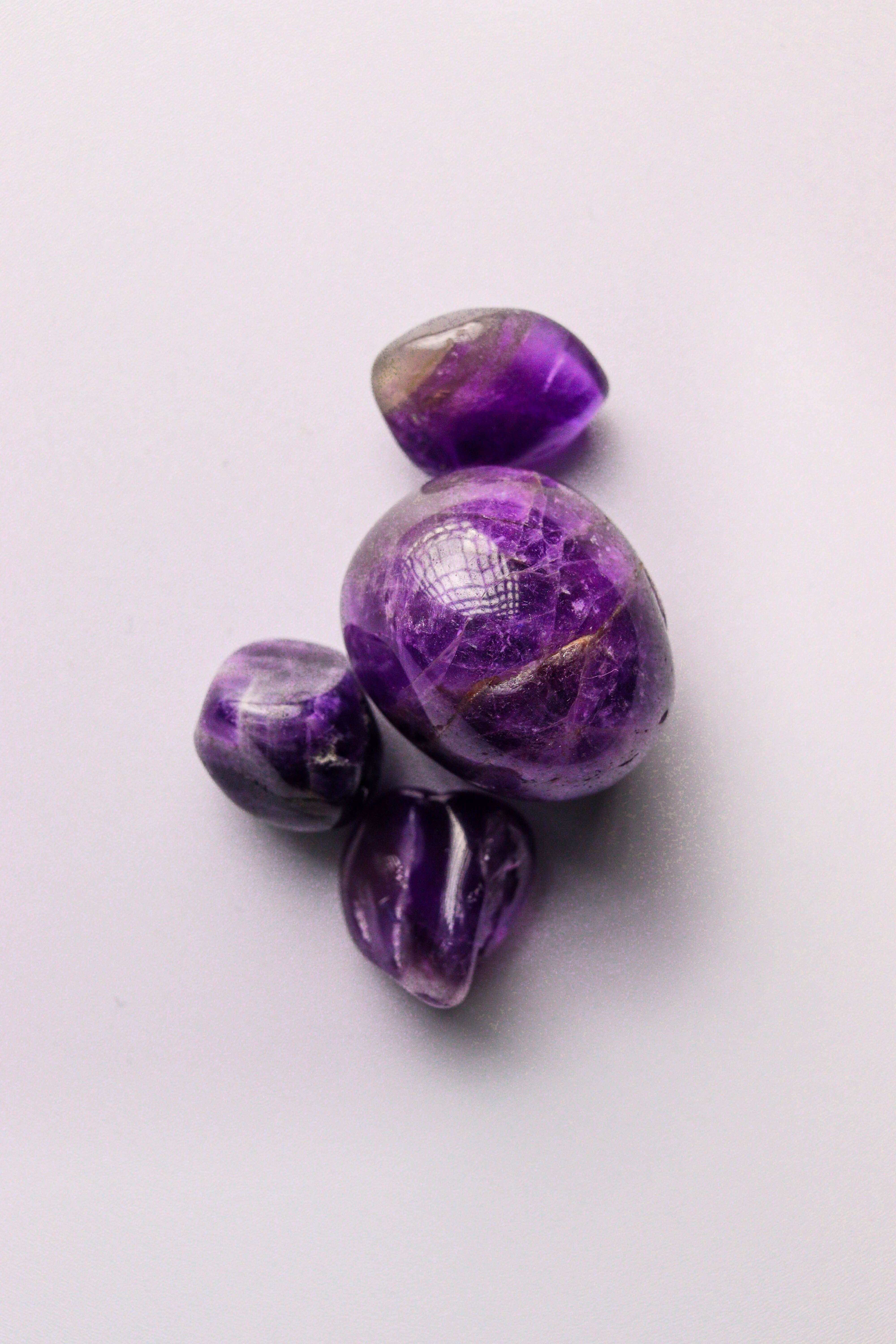 Fotomural Cuatro piedras de amatista pulidas sobre una superficie blanca que muestran sus profundos tonos púrpuras.