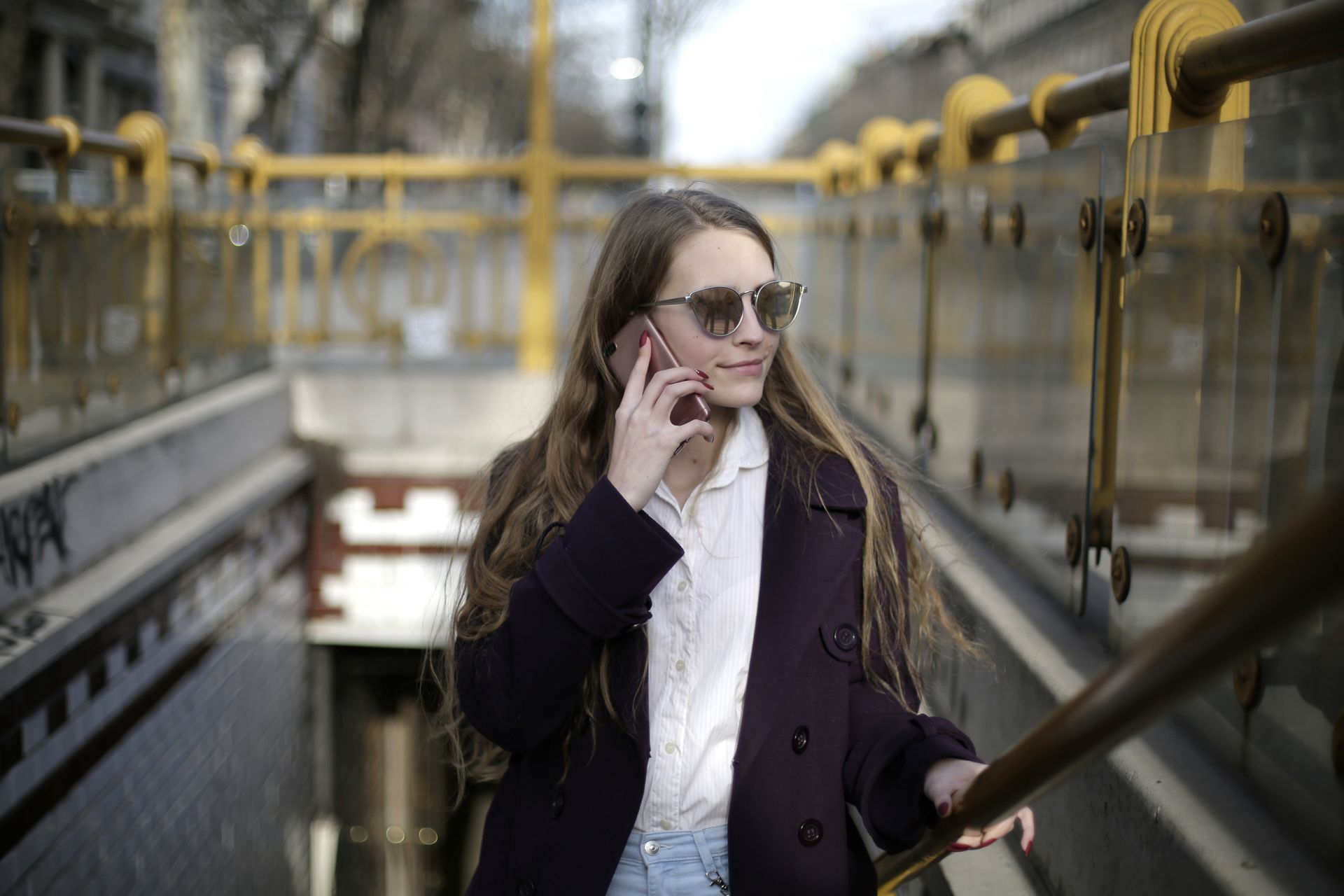 Young woman with sunglasses talking on smartphone near urban railing.