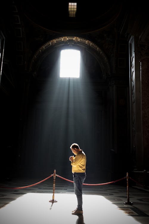 Unrecognizable man praying in church in sunlight