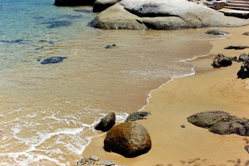 Free Tranquil beach scene featuring rocks, golden sand, and gentle ocean waves. Stock Photo