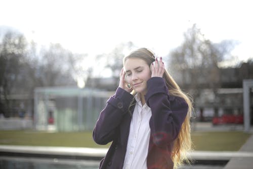 Woman in Violet Coat Holding White Headphones