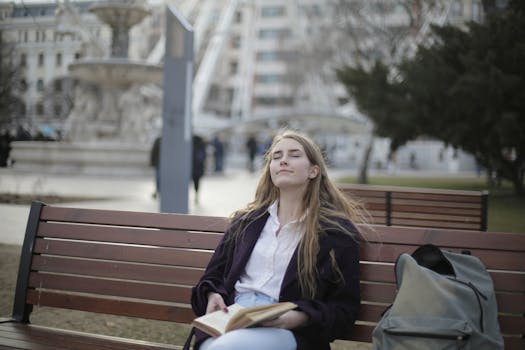 一位女士闭着眼睛，手里拿着一本书，在公园的长椅上享受放松的时刻