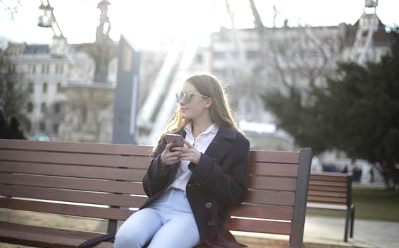 一位戴墨镜的女人在阳光明媚的公园长凳上发短信