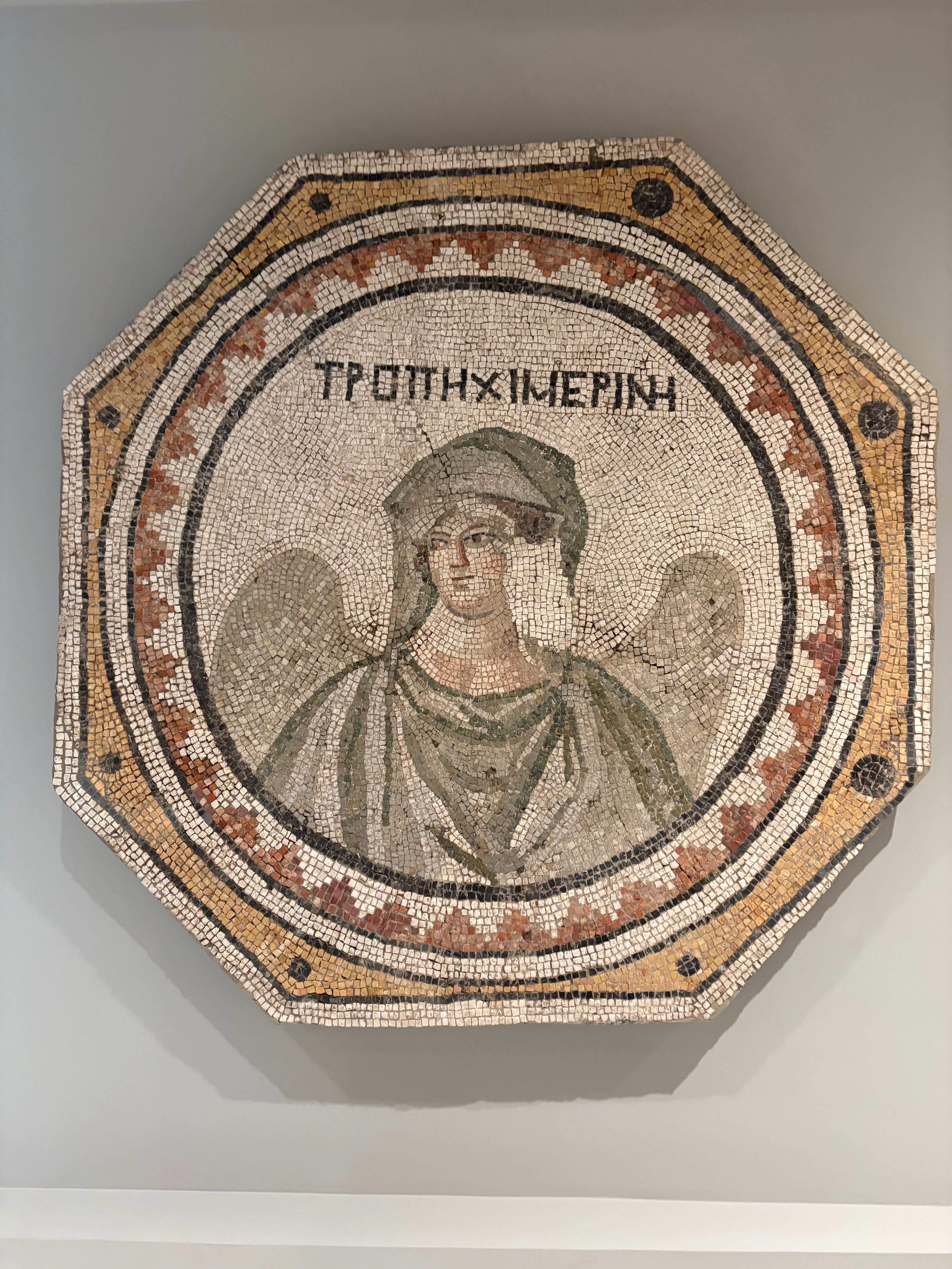 A detailed Roman mosaic displaying an angelic figure with Greek text, encapsulating ancient artistry.