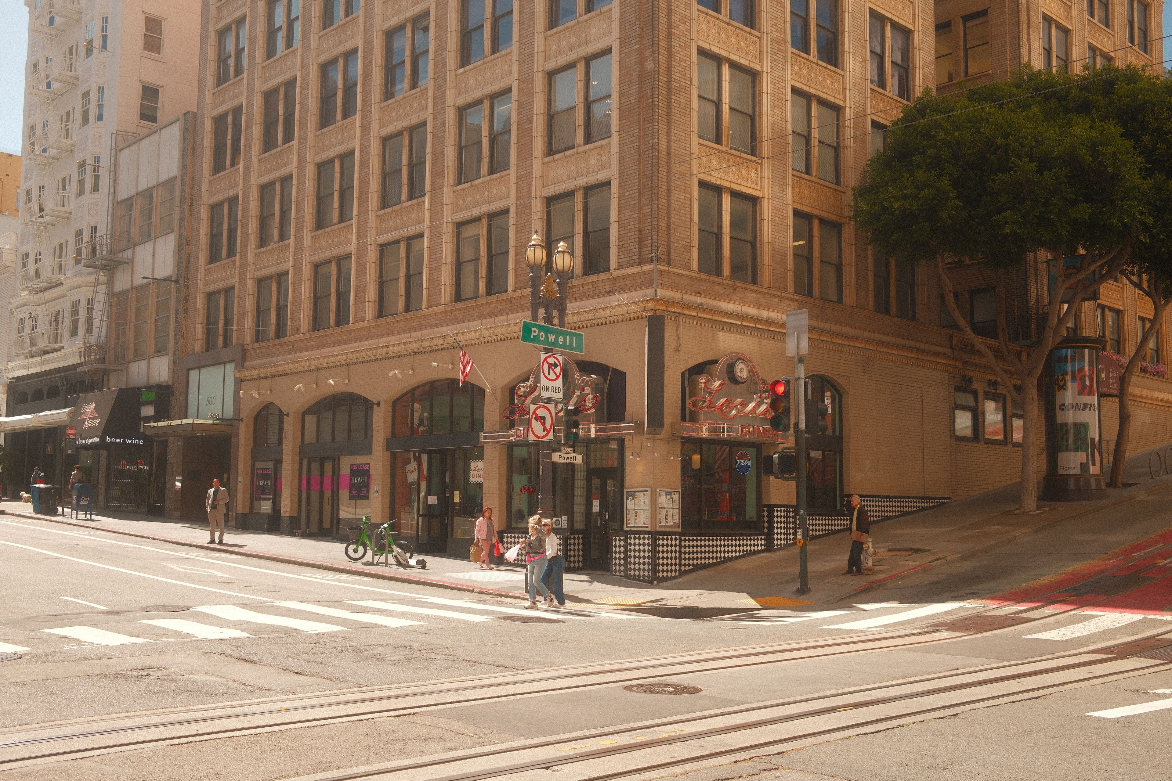 Daytime street corner of Powell and Market in San Francisco featuring a cityscape with pedestrians.