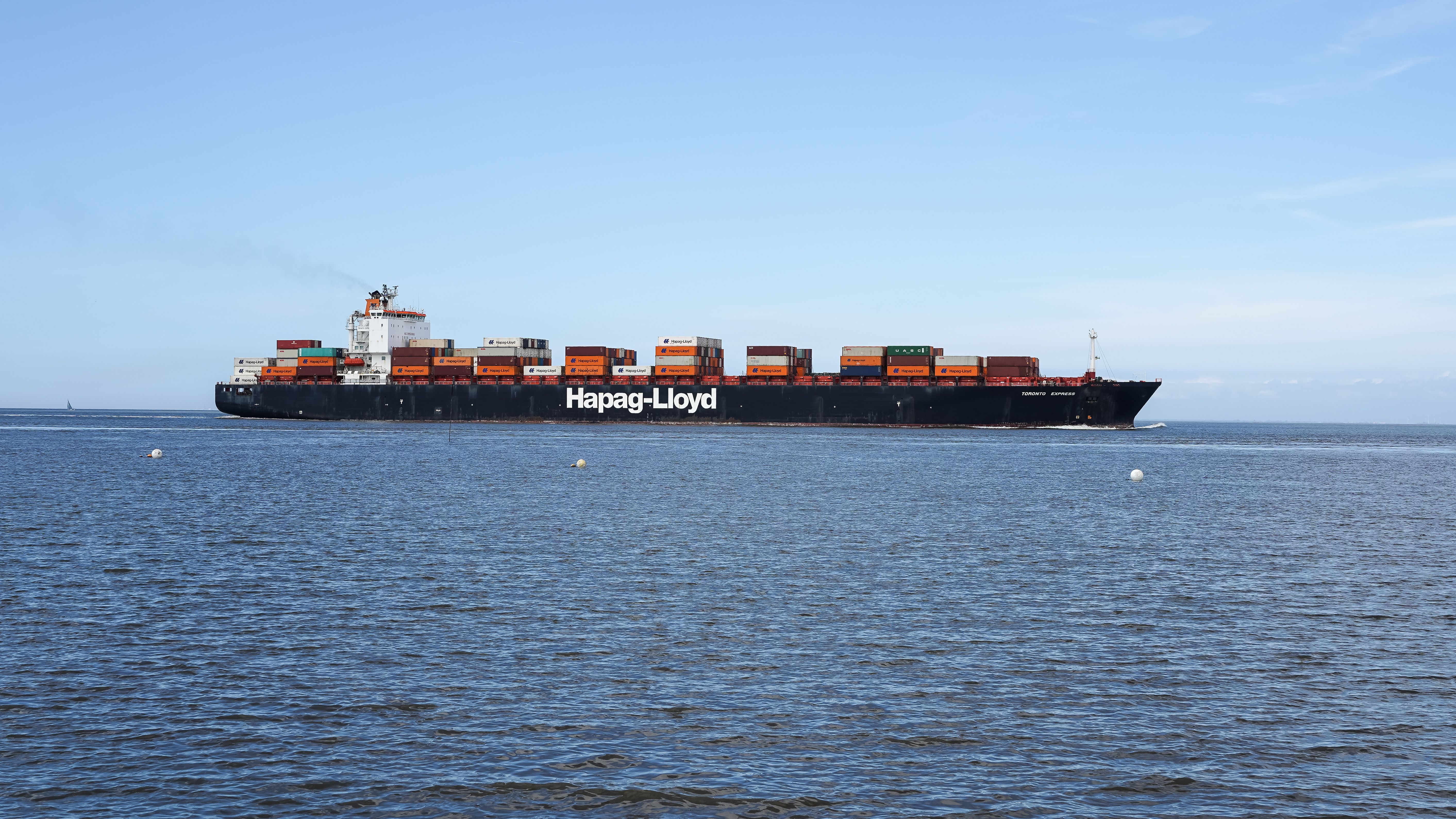 Container ship on Elbe River near Cuxhaven, Germany under clear blue skies.