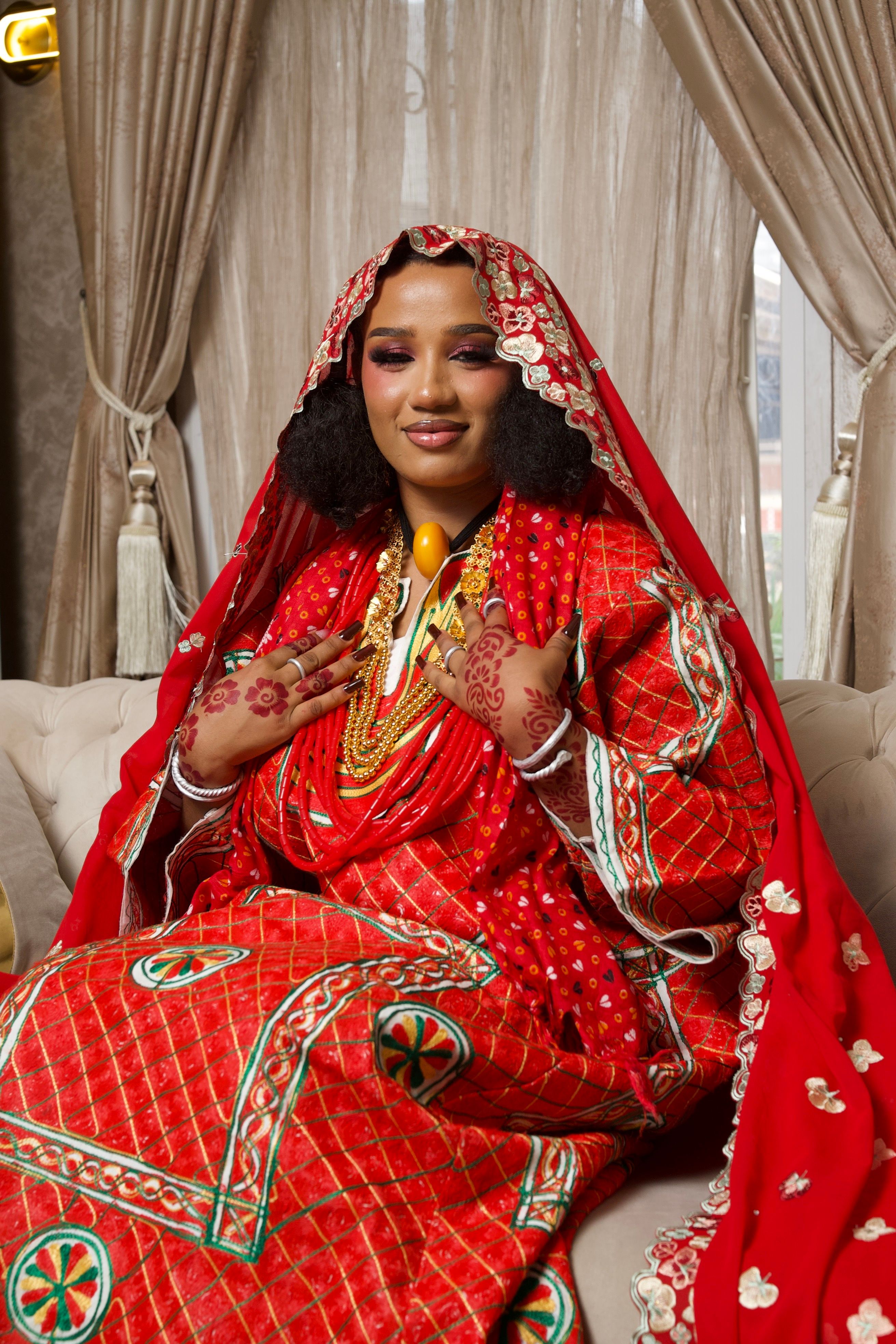 Beautiful Nigerian bride in a red ceremonial dress with henna art and gold jewelry.