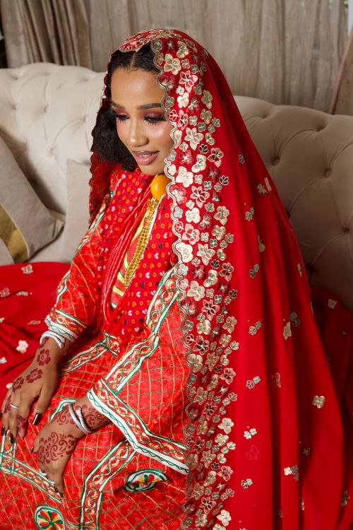 Free A stunning African bride in red and gold traditional attire with henna art, captured indoors. Stock Photo