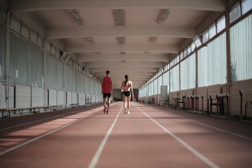 Back view of sportsman and sportswoman in activewear walking along running track in athletics arena during warming up before training