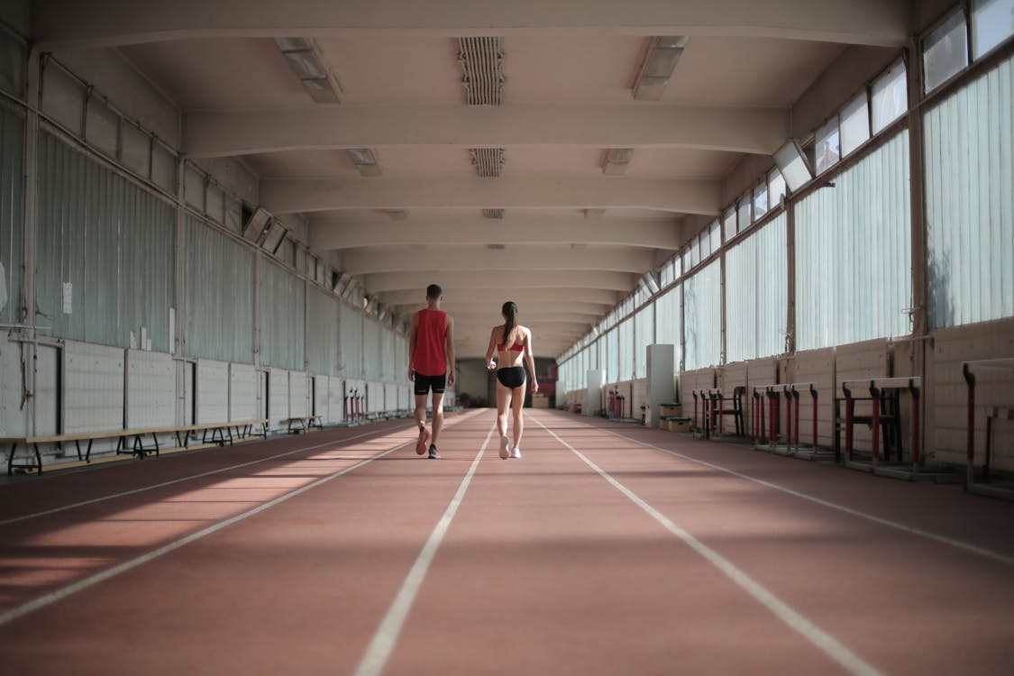 Free Back view of sportsman and sportswoman in activewear walking along running track in athletics arena during warming up before training Stock Photo