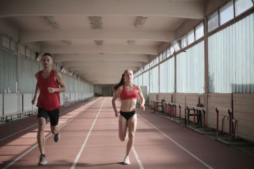Free Male and female athletes running on an indoor track, showcasing fitness and energy. Stock Photo