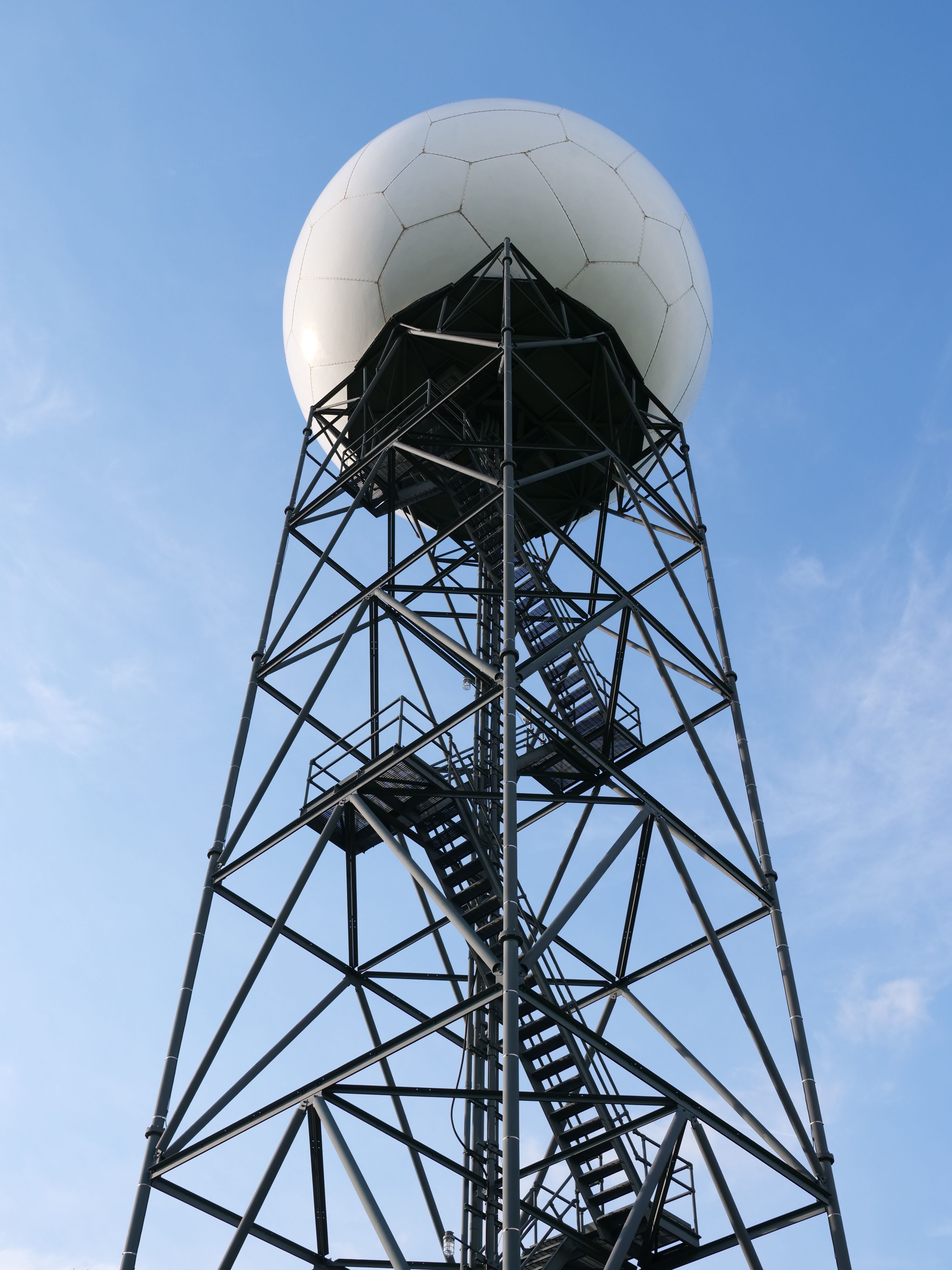Low angle view of a metal radar tower with a geodesic dome against a clear blue sky.