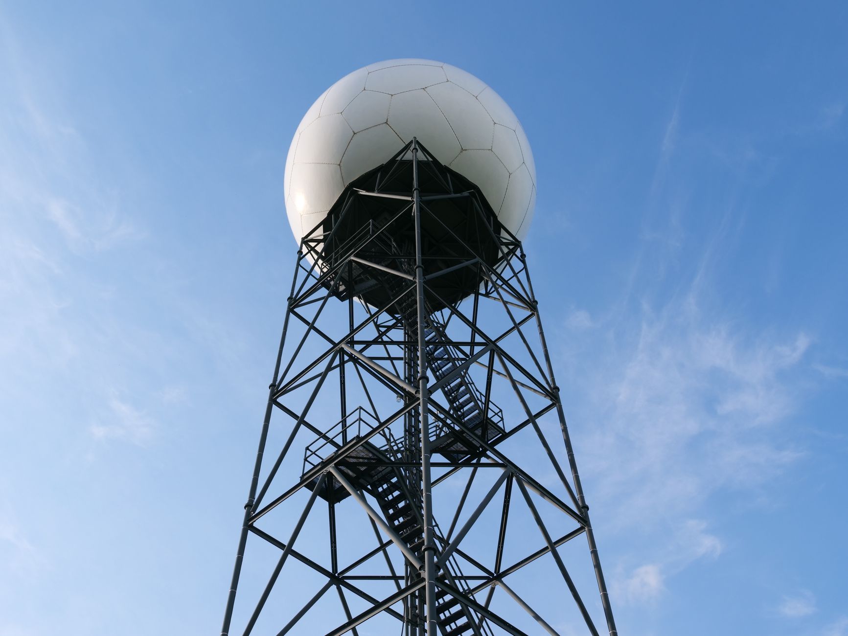 A weather radar tower featuring a geodesic dome rises against a clear blue sky, highlighting modern engineering.